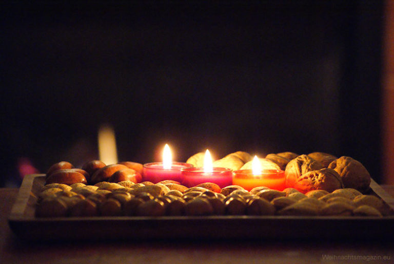a diplay on wooden tray with geometrically arranged nuts and red tealights