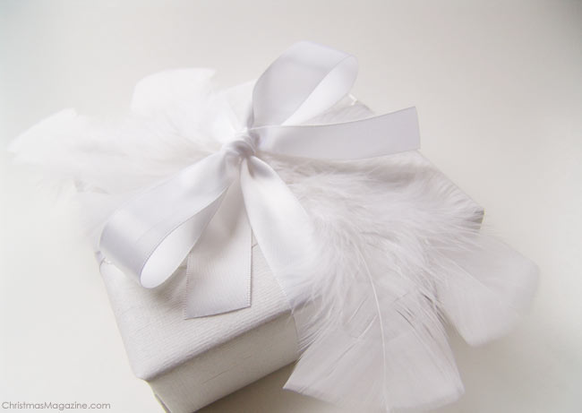 present wrapped in white with feathers and satin ribbon