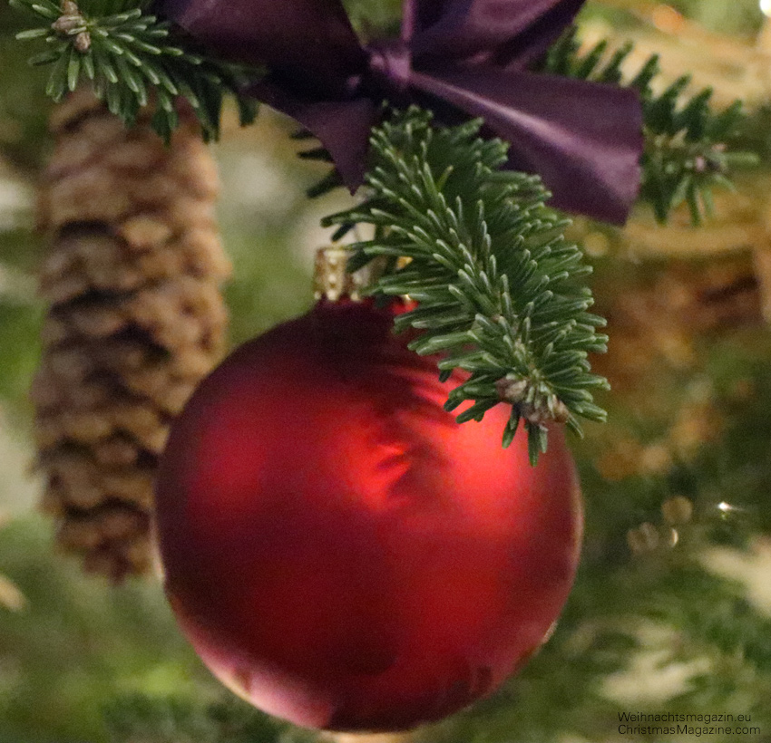 red bauble hanging on Christmas tree with purple bow