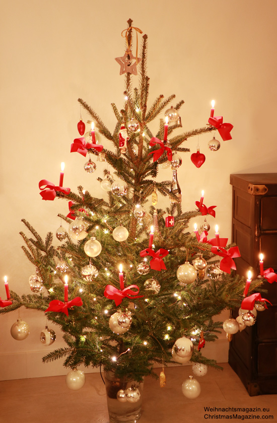 Christmas tree decorated in white with red bows and wax candles